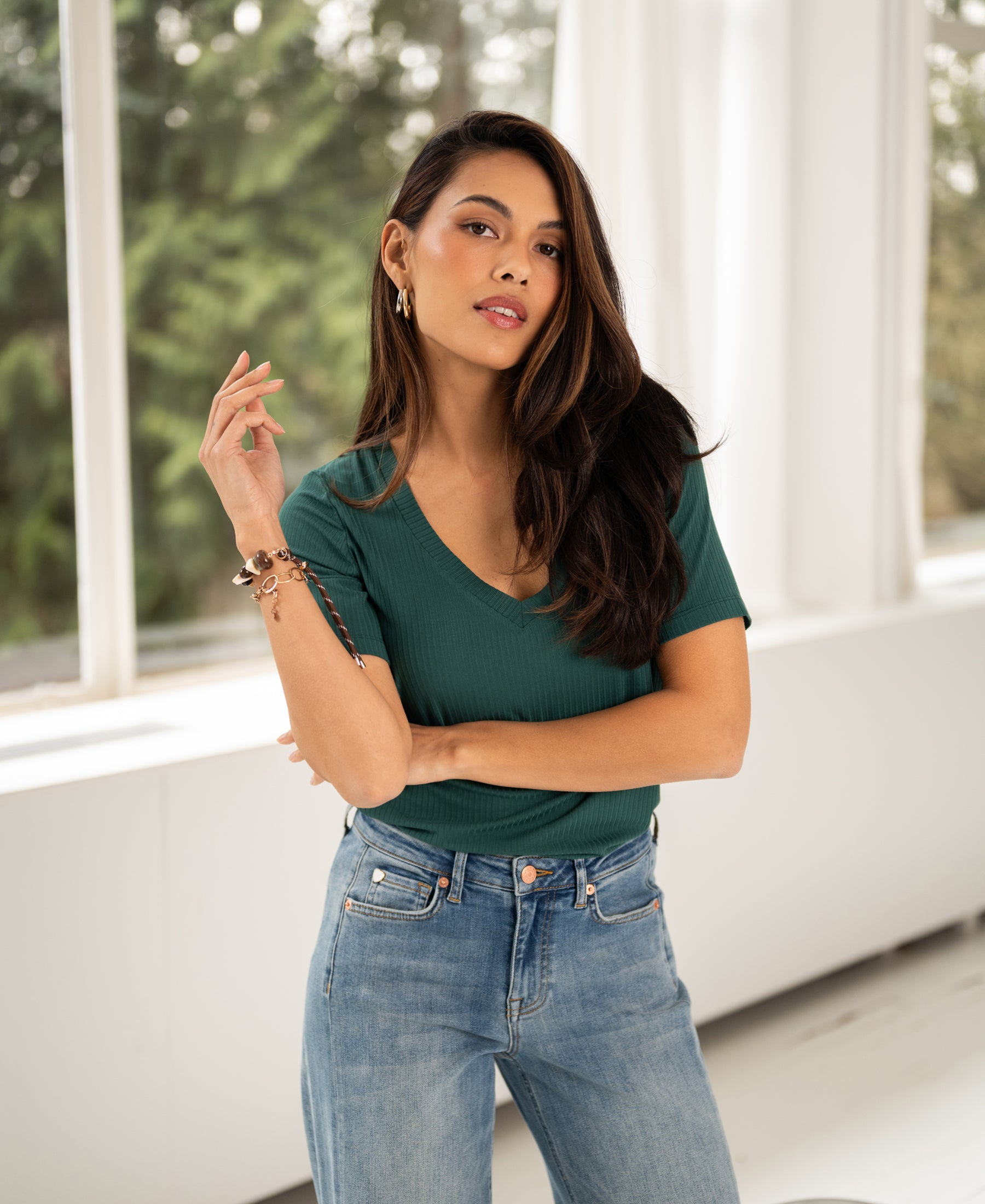 Woman wears the PLEIN PUBLIQUE Bamboo T-shirt in emerald green, indoors by large windows.