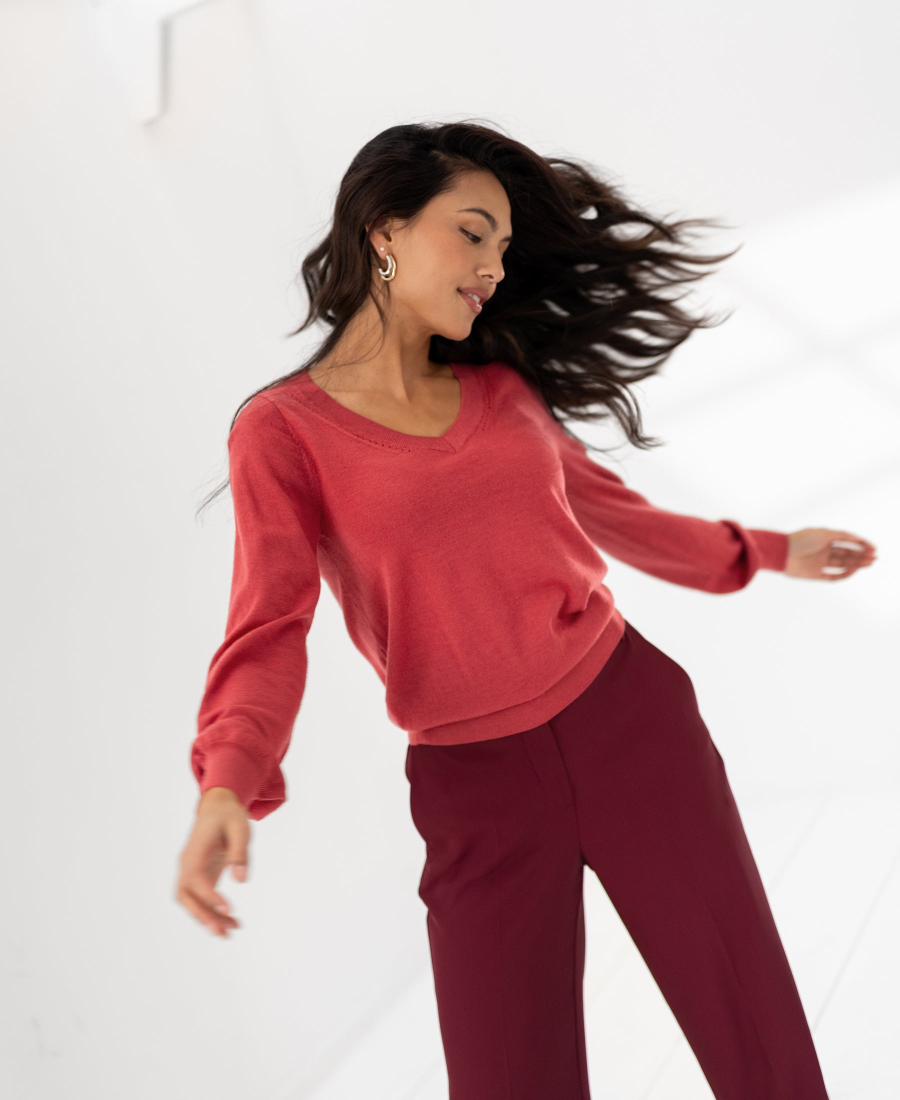 Woman wearing PLEIN PUBLIQUE Merino V-neck sweater LA VILLE Rouge, shown against a white background.