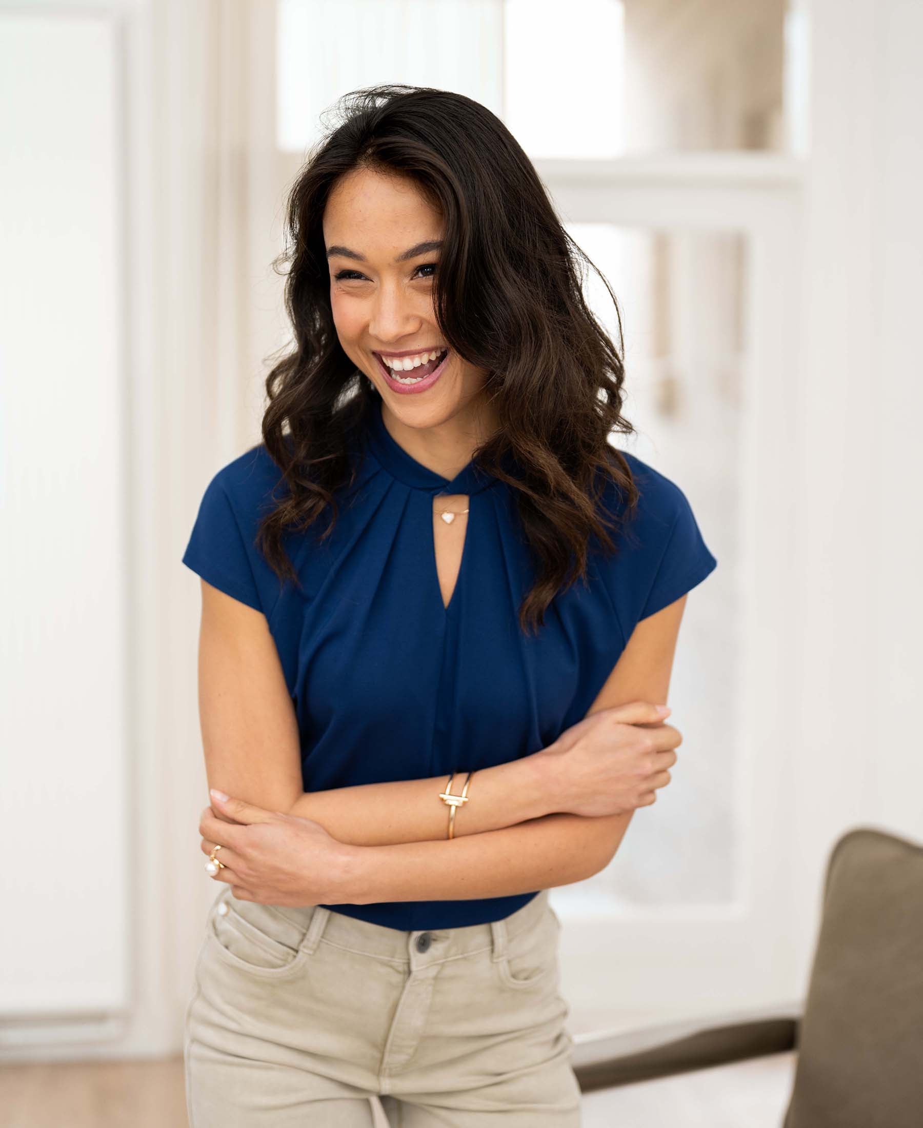 Sleeveless navy top in a relaxed fit, shown on a woman standing indoors with arms crossed.