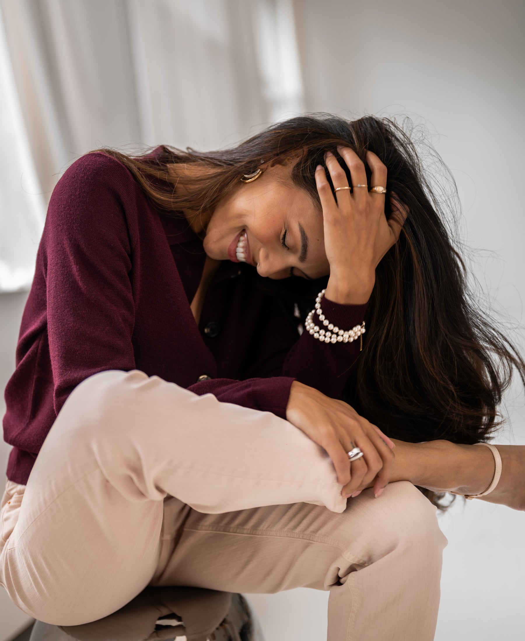 Woman in a Bordeaux red collared vest from PLEIN PUBLIQUE, sitting sideways and smiling.