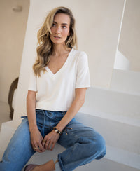 Woman wearing ivory PLEIN PUBLIQUE LA VOIX short sleeve stretch T-shirt, seated on white stairs, looking aside.