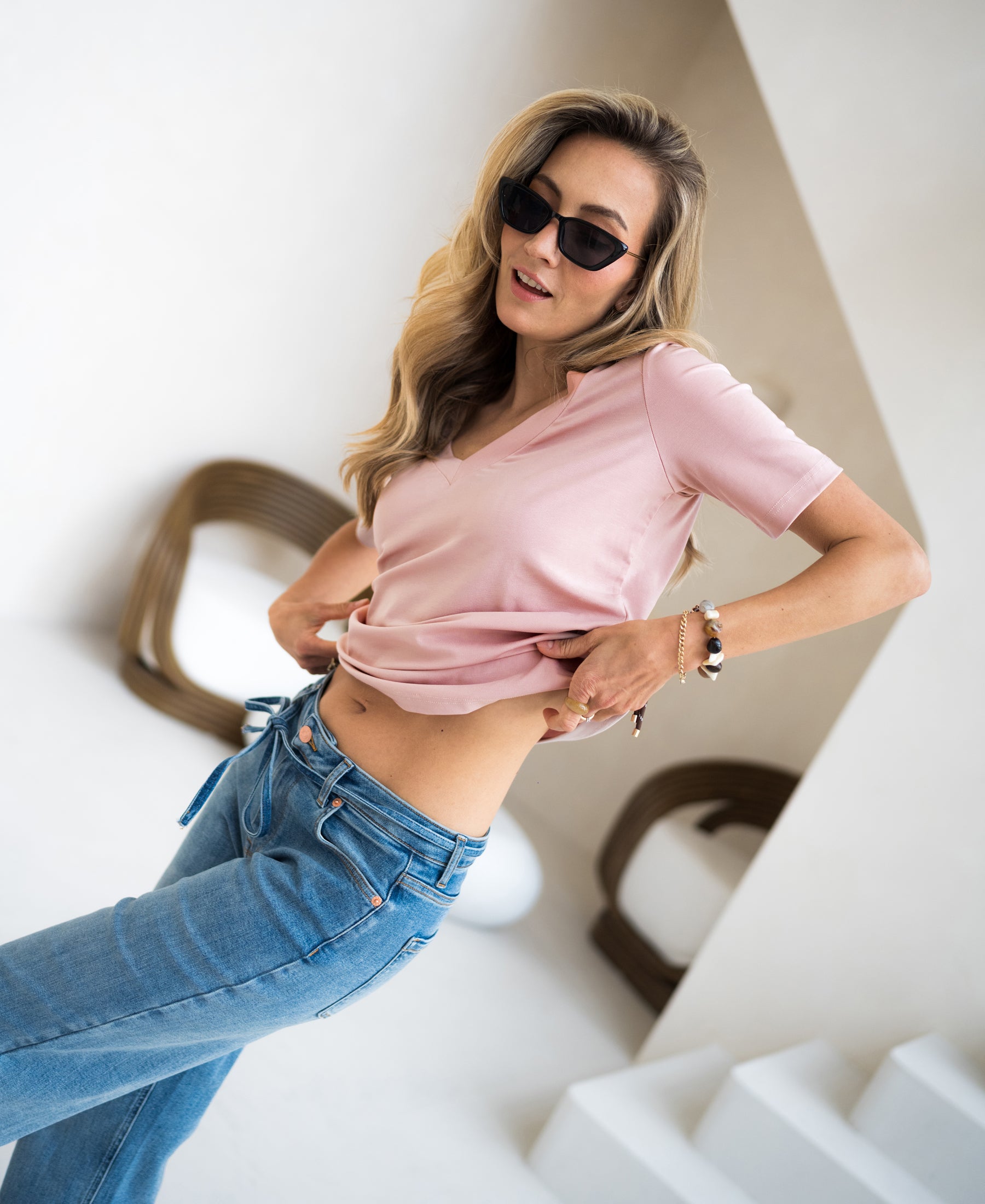 Woman indoors adjusts her pink PLEIN PUBLIQUE stretch short sleeve T-shirt.