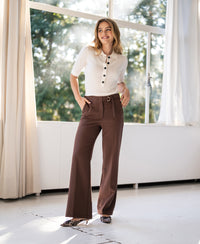 Woman wearing La Wende Cacao brown pants by Plein Publique, standing by large windows.