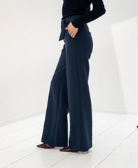 Person wearing dark blue Plein Publique LA WENDE trousers, hand in pocket.