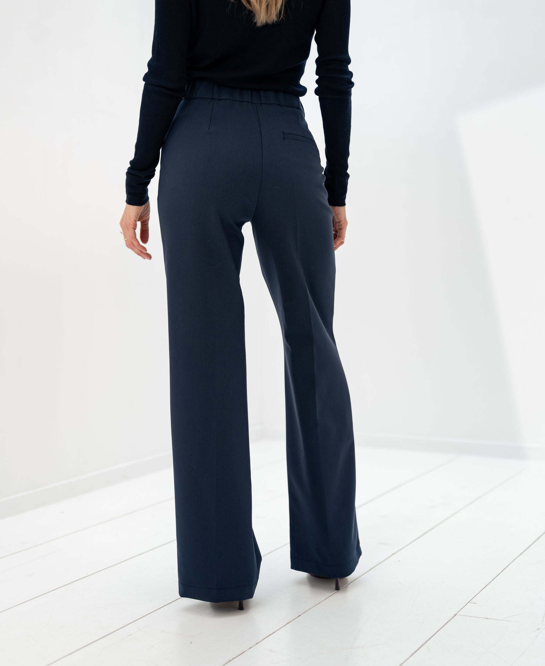 Dark blue PLEIN PUBLIQUE LA WENDE pants, shown from the back on a white floor.
