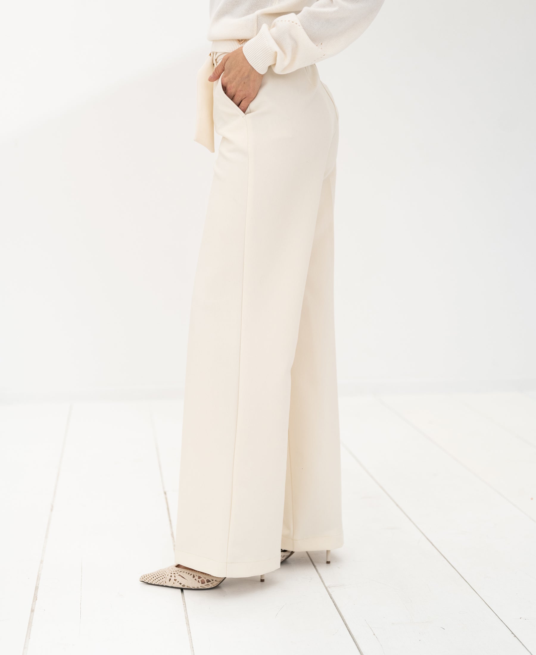 Cream-colored women's pants displayed on a person standing on a white wooden floor.