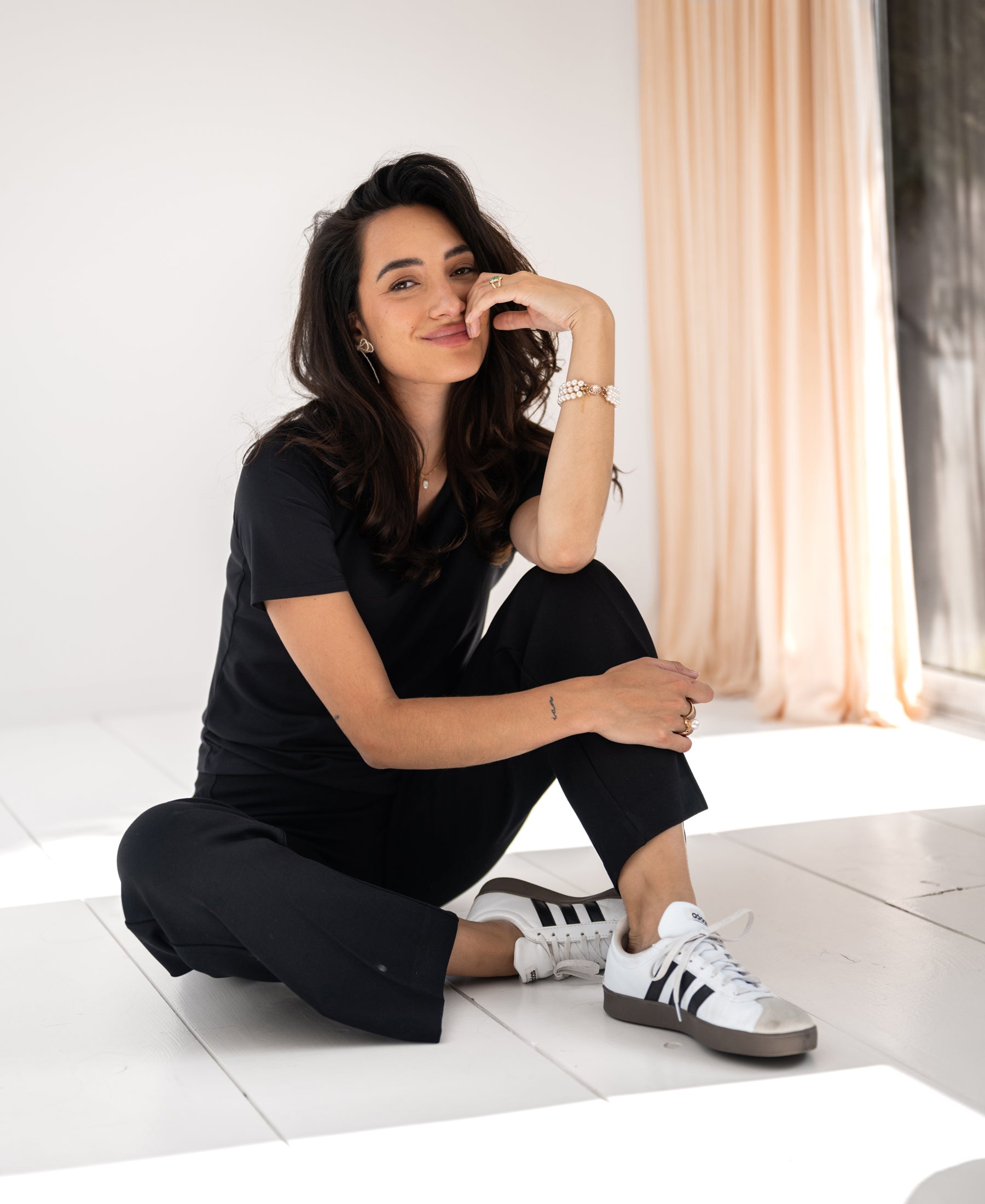 Woman wearing a black PLEIN PUBLIQUE Travel T-shirt LE FAVORY, seated cross-legged, light curtain in background.