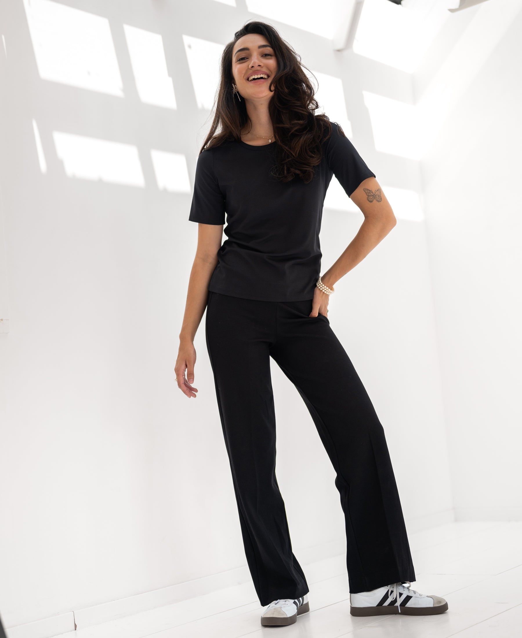 Woman wearing black PLEIN PUBLIQUE Travel T-shirt, LE FAVORY style, standing in a bright room.