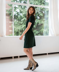 Woman wearing a dark green PLEIN PUBLIQUE button dress stands by large bright windows.