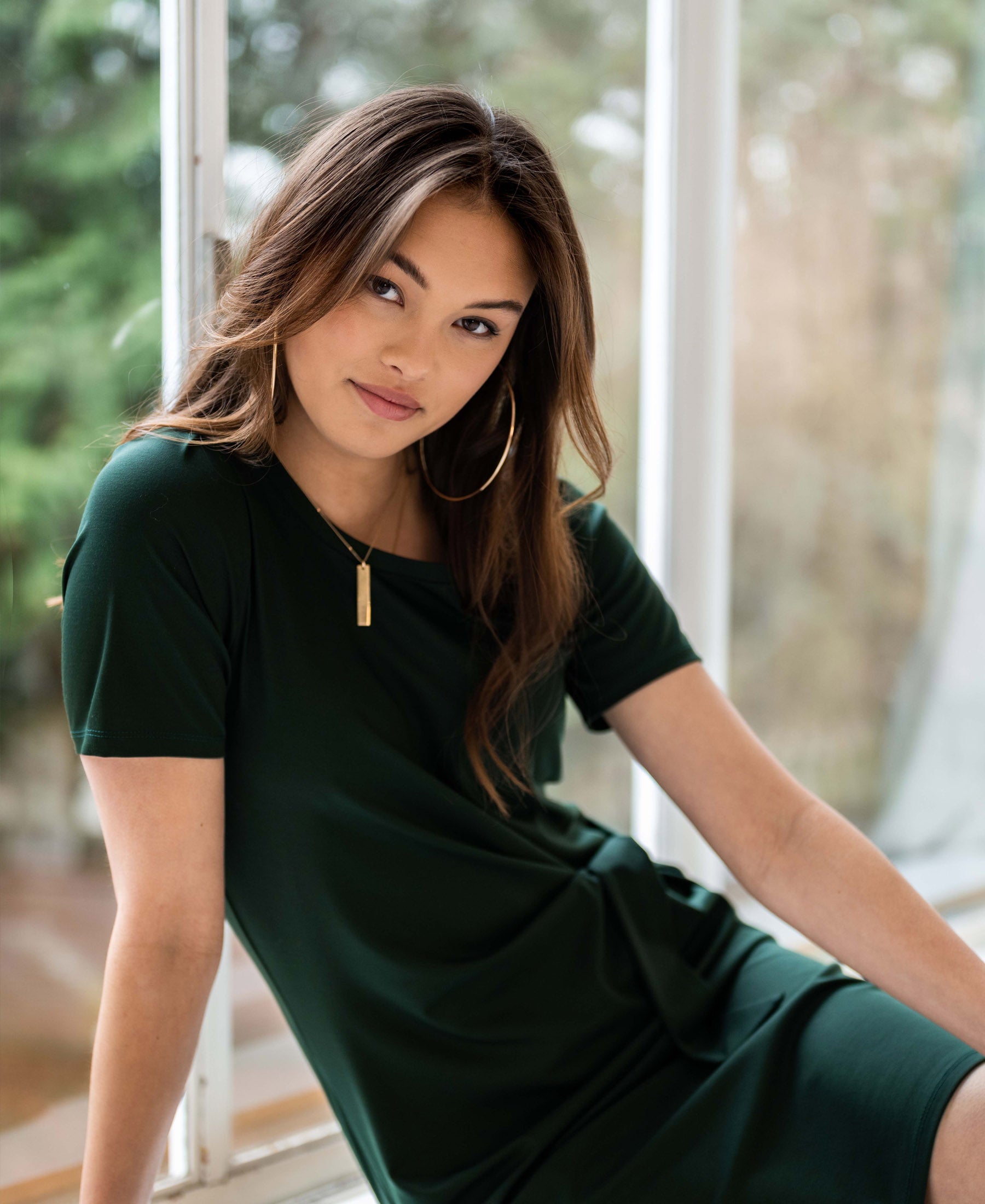 Dark green button dress displayed on a model seated by a window.